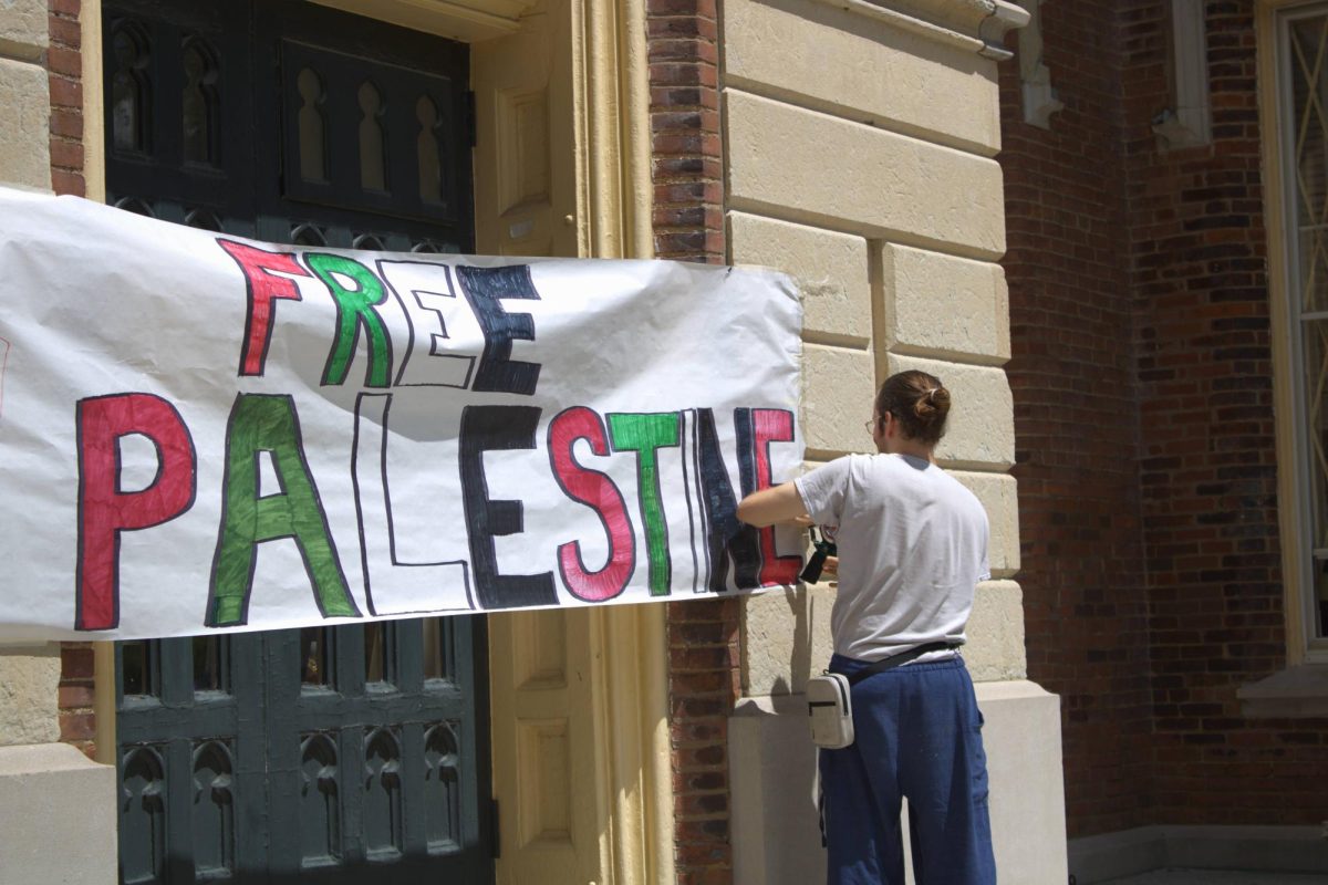 Kevin Cox, adjusting the Free Palestine banner at the threshold of Old Main